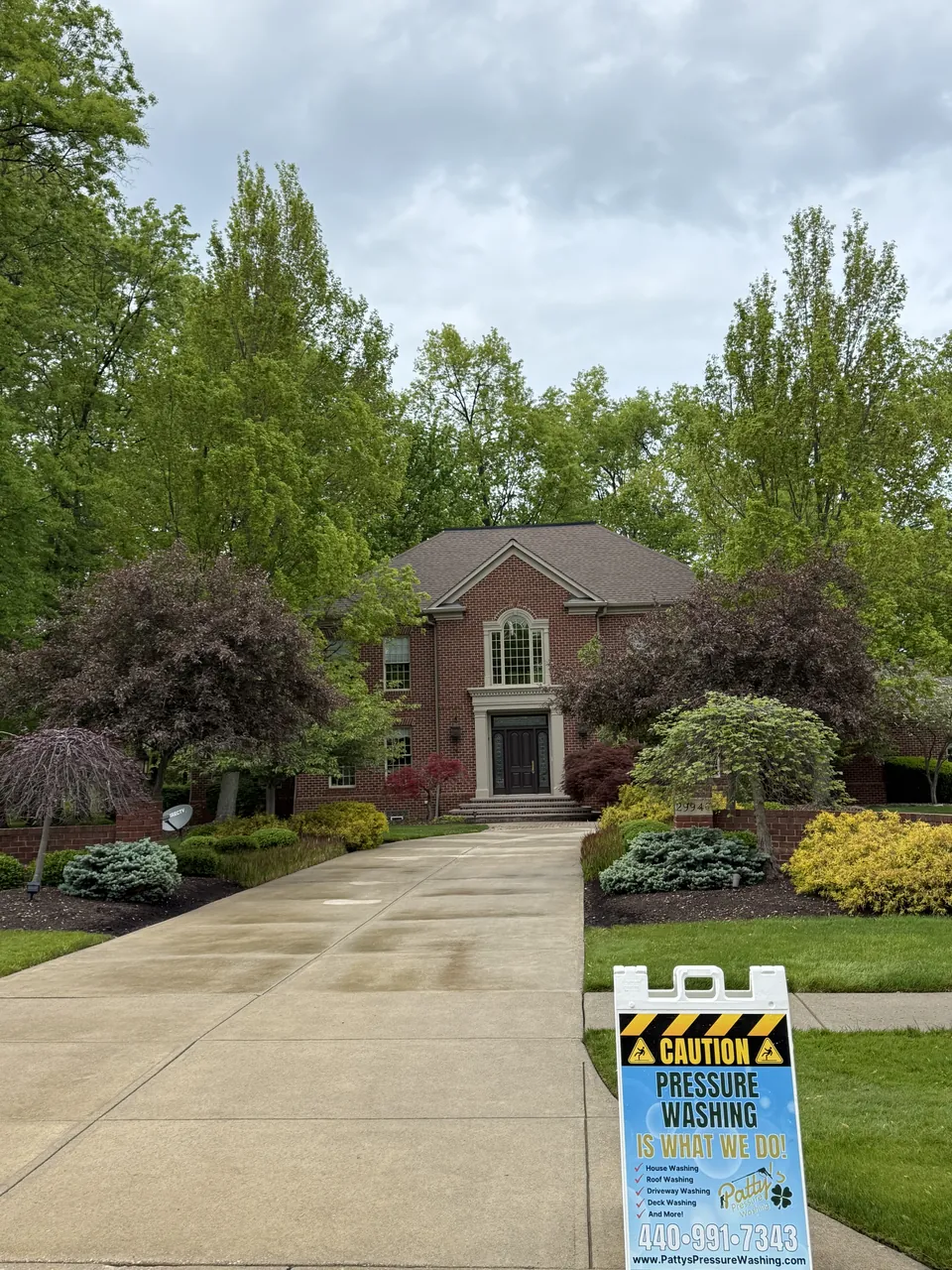 A cleaned concrete driveway sweeping up to a brick colonial, by Patty's Pressure Washing