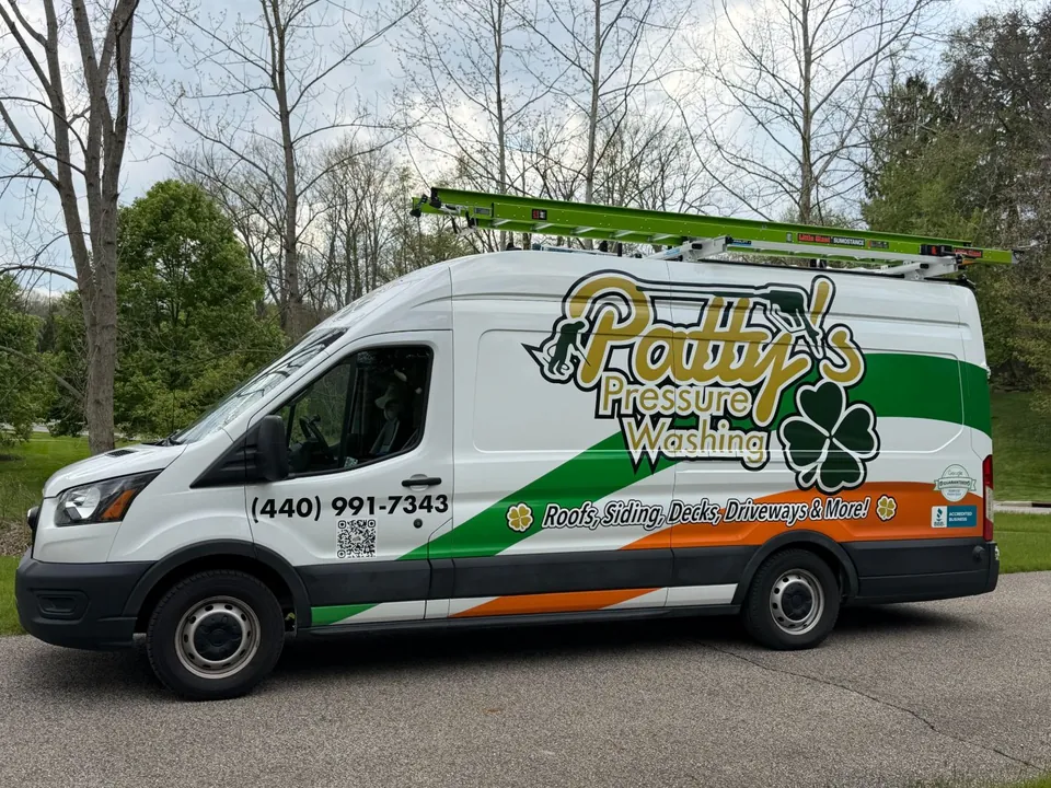 The Patty's Pressure Washing van, a white Ford Transit with the gold Patty's script, green shamrock and green-and-orange stripes, parked on a drive with ladders on the roof rack