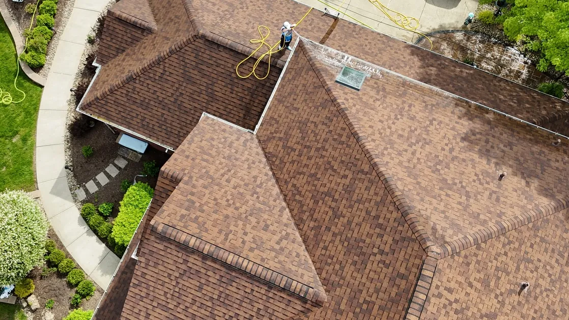 A cleaned brown shingle roof seen from above, with a technician on the ridge, by Patty's Pressure Washing