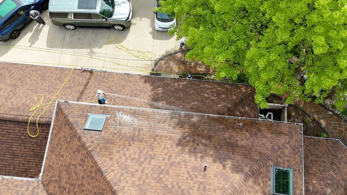 A brown shingle roof being soft washed from above, the treated band visible, by Patty's Pressure Washing