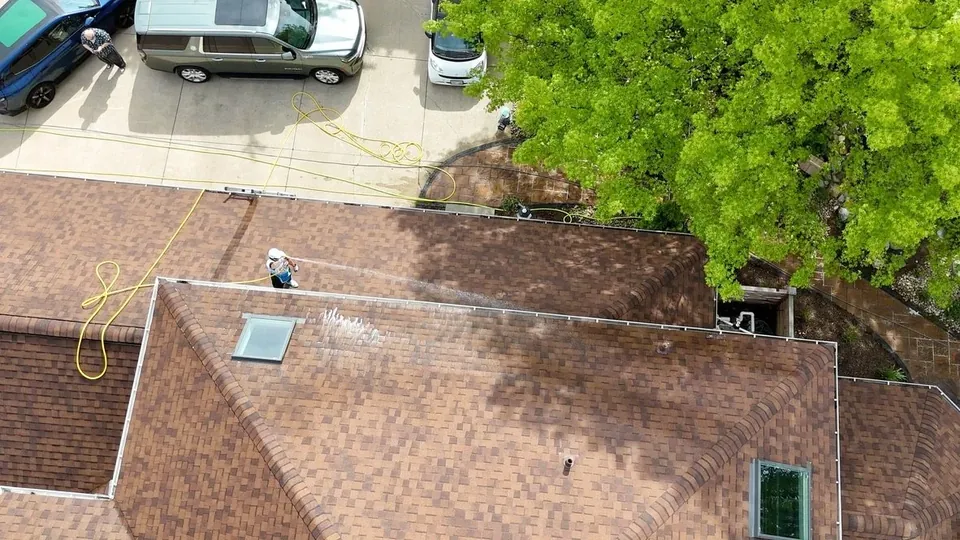 Aerial view of a Patty's Pressure Washing technician soft washing a brown asphalt-shingle roof